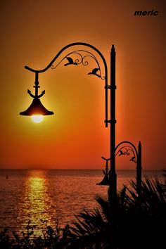 the sun is setting over the ocean with an iron lamp post and seagulls