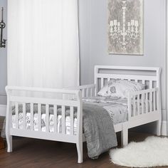 a white bed sitting in a bedroom next to a window with curtains on the windowsill