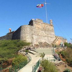 an old castle with stairs leading up to it and a flag flying high in the air