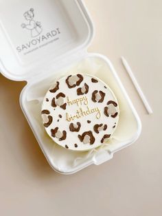 a white and brown cake in a plastic container with writing on the top that says happy birthday