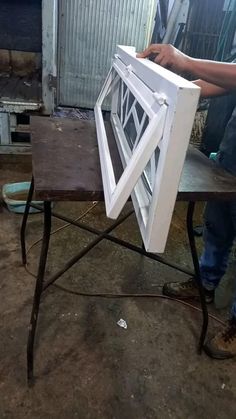 a man is holding up a window on top of a table in the process of being made