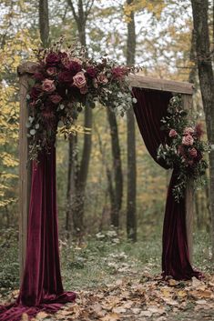 an outdoor wedding arch decorated with flowers and greenery in the fall forest, surrounded by fallen leaves