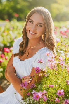 a woman in white dress sitting on a bench surrounded by wildflowers and smiling at the camera