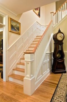 a clock sitting on the side of a wooden stair case next to a white banister