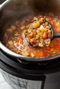 a ladle full of soup is being stirred into the crock pot with meat and vegetables