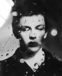 black and white photograph of a woman's face with rain drops on the window