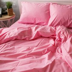 a bed with pink sheets and pillows on top of it next to a small table