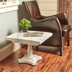 a small table with a magazine on it next to a brown chair and window sill