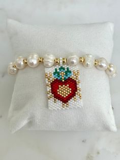 This Woven Heart Miyuki Beads Adjustable Bracelet is made with the following: Size & Material: - Features 8mm pearls and 4mm gold beads all strung on a cord  - The centerpiece showcases the Sacred Heart of Jesus, intricately crafted from small glass beads in white, red, gold, and turquoise. - The miyuki beads centerpiece measure 1'' x 1.25'' - The bracelet measures approximately 11'' long  - Adjustable cord for perfect fit The ideal gift for those devoted to the Sacred Heart of Jesus, perfect fo Heart Bracelet With Round Beads As Gift, Heart Beads Bracelet Gift, Heart Bracelet With Tiny Beads For Gift, Heart Shaped Beaded Bracelet With Letter Beads As Gift, Heart-shaped Beaded Pearl Bracelet Gift, Heart-shaped Beads For Valentine's Day Gift, Pearl White Pearl Bracelet With 8mm Beads As Gift, White Beaded Bracelets With Heart Charm As Gift, Pearl Heart Bracelet Gift