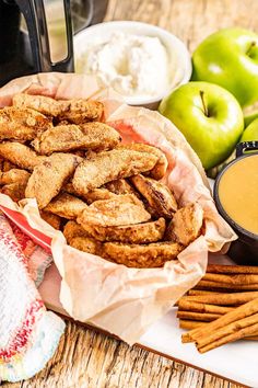 a basket filled with fried food next to some apples and cinnamon sticks on top of a wooden table