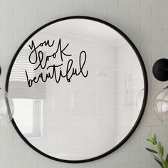 a round mirror with the words you look beautiful written in black on it next to a potted plant