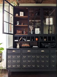 a black cabinet with lots of drawers and books on it's shelves in front of a window