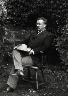 black and white photograph of a man sitting in a chair with a hat on his head