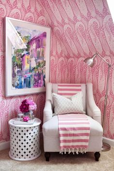 a white chair sitting next to a pink and white wall with a painting on it