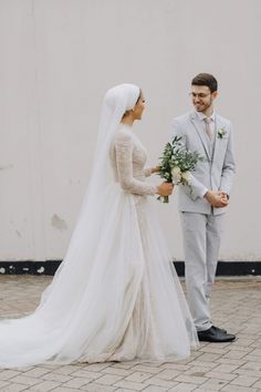 a bride and groom standing together in front of a white wall