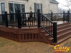 a wooden deck with black railings and hand rails next to a brick house in the background