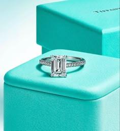 an emerald colored diamond ring on top of a blue box with diamonds around it and in the middle