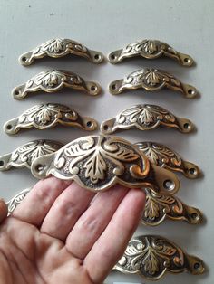 a hand is holding several antique brass drawer pulls