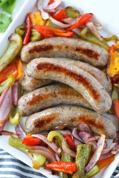 grilled sausages and peppers on a white platter with a striped towel in the background