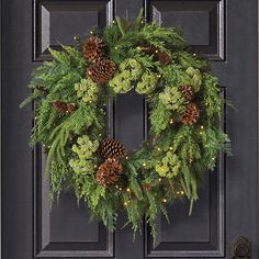 a christmas wreath with pine cones and evergreen needles on a black front door, decorated with lights