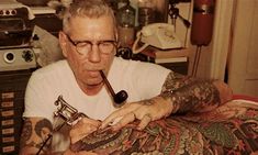 an older man with tattoos on his arms and arm holding a pipe in his hand