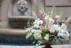 a vase filled with white and pink flowers sitting on top of a table next to a fountain