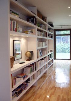 a room filled with lots of white bookshelves next to a doorway and wooden floors