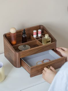 a person holding a wooden box with compartments on the table next to bottles and candles