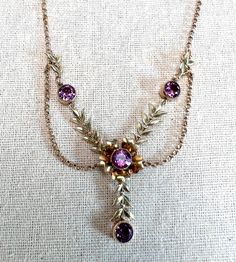 "Lovely gold purple paste festoon necklace with a gold filled triple link chain. This was made by Carl Art which was in business in the 1940s and 50s.  The central flower has laurel leaf segments connecting it to other stone.  It has articulated joints so the necklace will move slightly when you do.  Unique mid century piece. CONDITION:  In very good vintage condition. No obvious faults other than wear in keeping with age and use. HALLMARKS:  1/20 12K GF CA METAL: Gold filled GEMS:  Four round p Festoon Necklace, Art Nouveau Necklaces, Laurel Leaf, Heart Padlocks, Princess Ring, Colorless Diamond, Art Nouveau Jewelry, Art Nouveau Style, Treasure Box