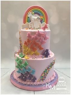 a three tiered cake decorated with rainbows, stars and a unicorn on top