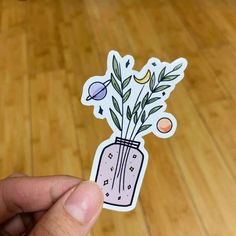 a hand holding a sticker with flowers in a vase