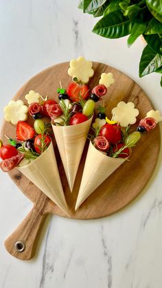 three cones filled with fruit and veggies on top of a wooden cutting board