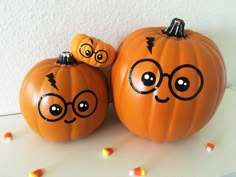 two pumpkins with faces drawn on them sitting next to each other in front of a wall