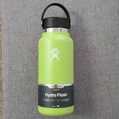 a green hydro flask water bottle hanging on a gray fabric wall with the words hydro flask printed on it