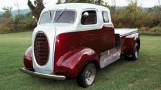 an old red and white truck parked in the grass