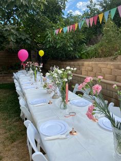 a long table set up with plates and vases filled with flowers, candles and balloons