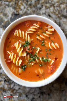 a white bowl filled with pasta soup on top of a granite counter topped with parsley