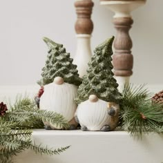 christmas decorations with pine cones and evergreens on the mantle mantel, including two white ceramic gnome figurines