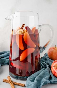 a pitcher filled with apples and cinnamons sitting on top of a table next to other ingredients