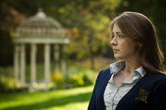 a woman standing in front of a gazebo looking off into the distance with trees and grass behind her