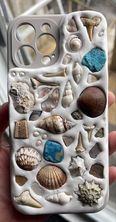 a person holding up a cell phone case with shells on it