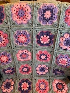 a crocheted granny blanket with pink, purple and blue flowers on it sitting on a chair