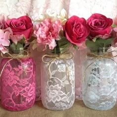 four vases with pink and red flowers are lined up against a white lace curtain