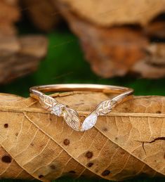 a gold ring with two leaves on it sitting on top of a leafy surface