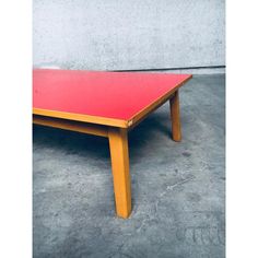 a red table sitting on top of a cement floor next to a gray concrete wall