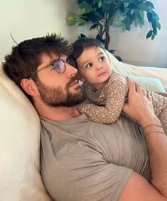 a man laying on top of a white couch holding a small child in his arms