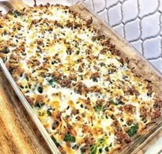 a casserole dish with broccoli, cheese and meat in it on a wooden table