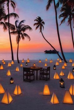 a table and chairs are set up on the beach at sunset with palm trees in the background