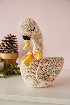 a crocheted duck with a yellow bow on its head is shown next to a pine cone