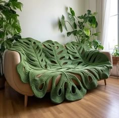 a couch covered in green crochet sits on a hard wood floor next to a potted plant